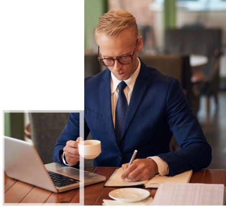 A professional in a suit working on computing assignments with a laptop and notebook in an office setting.